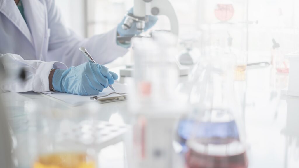 A,Scientist,Hands,Writing,On,A,Clipboard,In,Laboratory,With