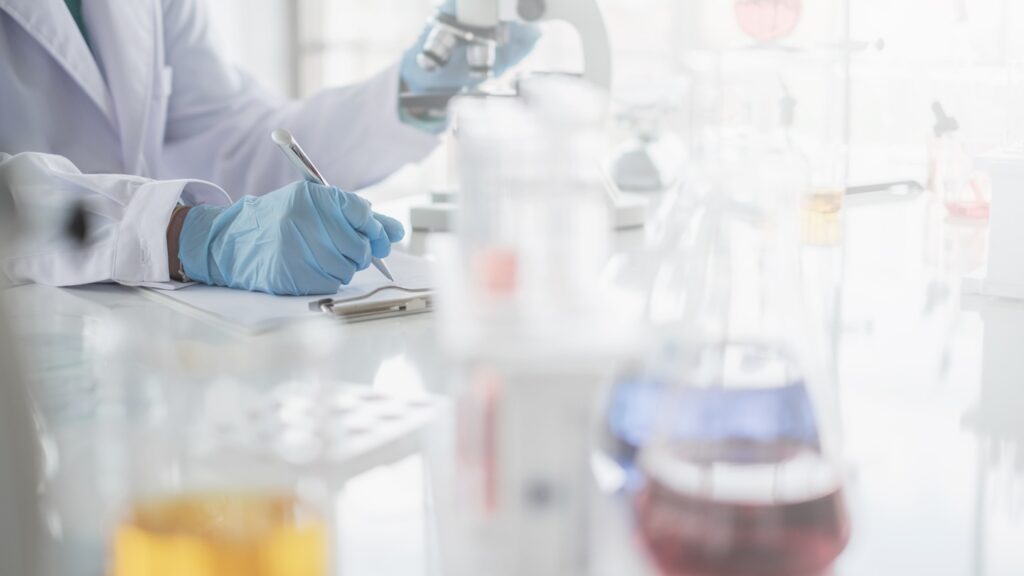 A,Scientist,Hands,Writing,On,A,Clipboard,In,Laboratory,With